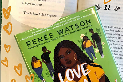 Book with a green cover and illustrations of a young couple. Title: Love is a Revolution by Renee Watson. Lines from the book are highlighted in the background and surrounded by yellow hearts. (Links to Teen Instagram page)