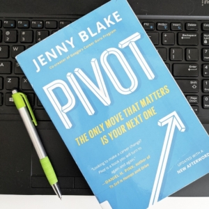 A light blue book with white and green lettering lies on a computer keyboard. The book is Pivot by Jenny Blake