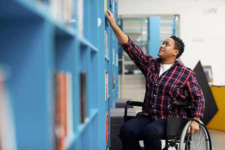 Person in a wheelchair reaches for a law book in the law library (Links to the Law Library page)