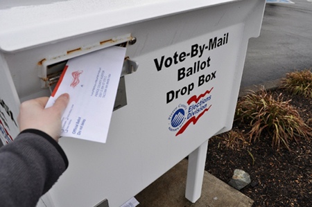 Person dropping a ballot in a ballot drop box at the library (Links to voter point of assistance information)