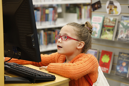 Child with glasses looks excitedly at the computer screen in the library