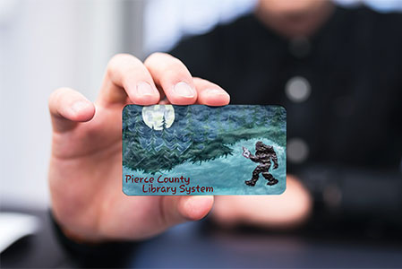 Person holding a library card designed by a student in the Library Card Design Contest (Links to Design Contest details)