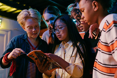 Group of teens looking at a book (Links to teen reading options)