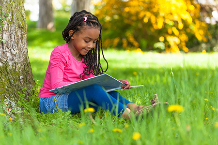 Child reading a book outside in the grass